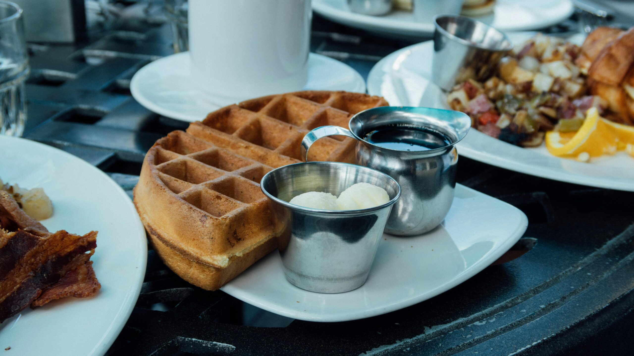 Close-up of waffles served with syrup and butter on a white plate, perfect breakfast setup.