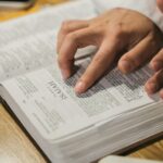 Close-up of hands reading a Bible, focusing on Isaiah passage, in an intimate indoor setting.
