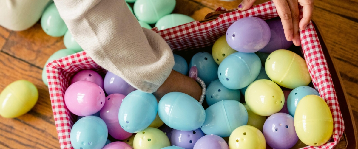 Child's hands reaching into a basket of colorful Easter eggs indoors.