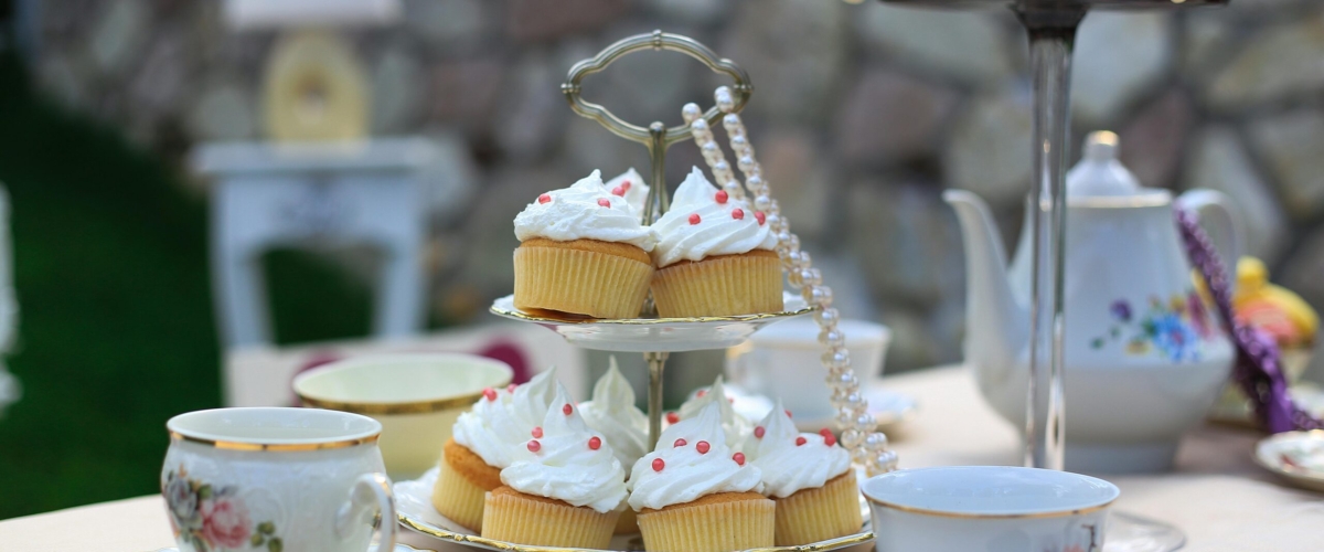 Charming tea party setup with cupcakes and porcelain tea set outdoors.